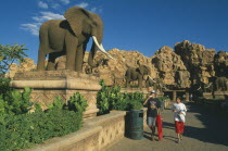 Tourist visitors on avenue lined with statues of elephants.