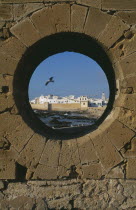 Fortified coastal town framed in circular opening in wall.