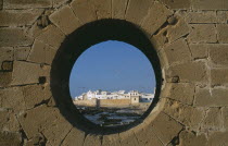 Fortified coastal town framed in circular opening in wall.