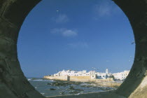 Fortified coastal town framed in circular opening in wall.