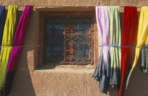 Detail of window with decorative metal screen set into wall with colourful lengths of dyed fabric hanging at each side. Colorful