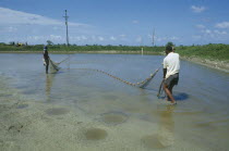 Two men pulling in a net in the pool at the fish farm project