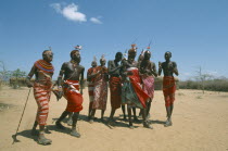 Samburu men and woman in traditional dress dancing in barren landscape.