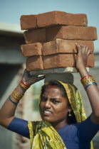 Woman carrying pile of bricks on her head