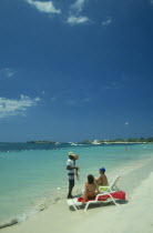 Man selling lobster to tourists on beach sitting on sun loungers by the water