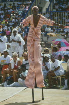 Stiltman in pink and white at traditional harvest festival to celebrate bringing in the sugar cane crop