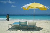 Tourist couple walking on beach by water past umbrella and sun loungers