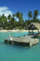 Boat jetty with tourist sitting down and the beach behind with people swimming and sunbathing