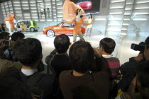 Tokyo Auto Show  at the Daihatsu exhibit  young men focus cameras on a young female model on a stage.