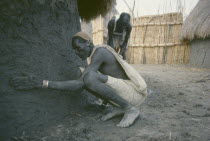 Shilluk man plastering exterior wall of mud hut.