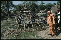 Local guru or holy man on village tour inspecting frame of hut waiting to be thatched.