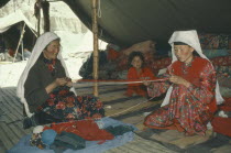 Kirghiz women winding wool inside yurt watched by young girl. Ger