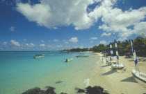 The beach at the Mauritius Hotel. People next to yachts with blue and white sails.