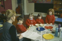 Nursery School children with teacher gathered around table taking part in art class.kindergarten