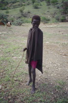 Portrait of young Masai boy with goats grazing in the background.