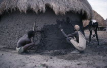 Shilluk men using mud to plaster the wall of a hut.