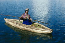 Uros woman on reed boat rowing to floating island.