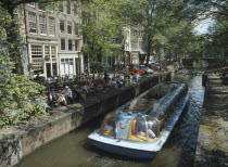 Glass roofed tourist boat passing canal side cafe on the Lelegracht canalNetherlands