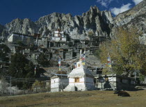 Village near Manang.  Flat roofed stone houses and stupa hung with prayer flags with steep cliffs behind.