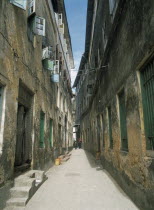 Stone Town.  Quiet  narrow street lined with houses with plaster walls and shuttered windows.  Two women at the far end.