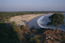 View along the beach and coastline with people standing by tree on rocky promontory in the foreground