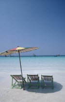 Empty sun loungers and umbrella on beach with boats moored just off shore