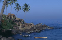 Coastal scene with coconut palms on rocky promontory and men in boats beyond