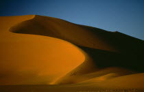 Sand dune partially cast in shadow against blue sky