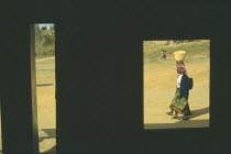 Women carrying baskets framed by window of building in deep shadow.