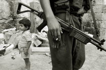 Israeli soldier with rifle and cigarette relaxes in the Arab Quarter  small boy standing behind.