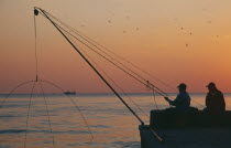 Fishermen on harbour wall at sunset with distant fishing boat.near Grosseto