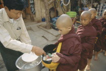 Giving early morning Alms to young Monks queuing up at side of road. Myanmar