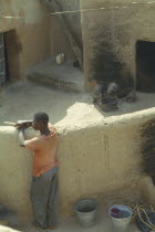 Young man standing against wall in traditional Gurunsi village.