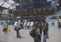 Train station interior with people gathered around departure board.