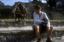 Tourist smoking a cigarette with Coati walking along the wall behind in the main Plaza