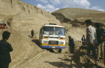 Bus stuck in earth along the main road with people standing by the sides of the dirt track