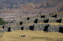 Looking down on visitors walking between the Inca walls and Cusco in the distance.