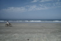 Cyclist riding along sand of the empty beach with waves rolling on to the shore