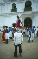 Procession outside village church with statue of Christ being carried out of church watched by shoeless old man