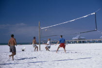 People playing beach volleyball with small pier in the background