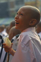 Laughing novice monk dressed in white holding a lotus flower during a mass ordination ceremony