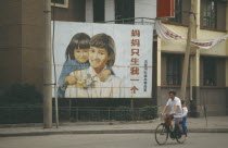 Man with child passenger cycling past birth control poster with image of female child.