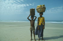 Boy and girl from Karnataka on beach carrying fruit and drinks to sell to tourists