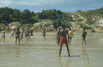 Men playing football on the wet sand of the beach with sticks for goalposts