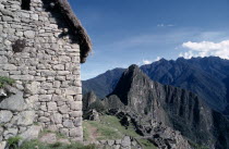 View of the side of a stone built thatched house with ruins beyond