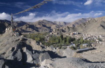 Prayer flags blowing in the wind on top of rocks in the foreground overlooking town surrounded by mountains