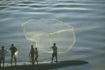 Fishermen standing on long boat casting net