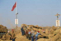 People threshing paddy crop. Red Communist Flag flying