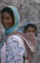 Portrait of Kurdish mother carrying child in sling on her back.