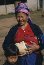 Mother breastfeeding baby while standing with older child at her side.